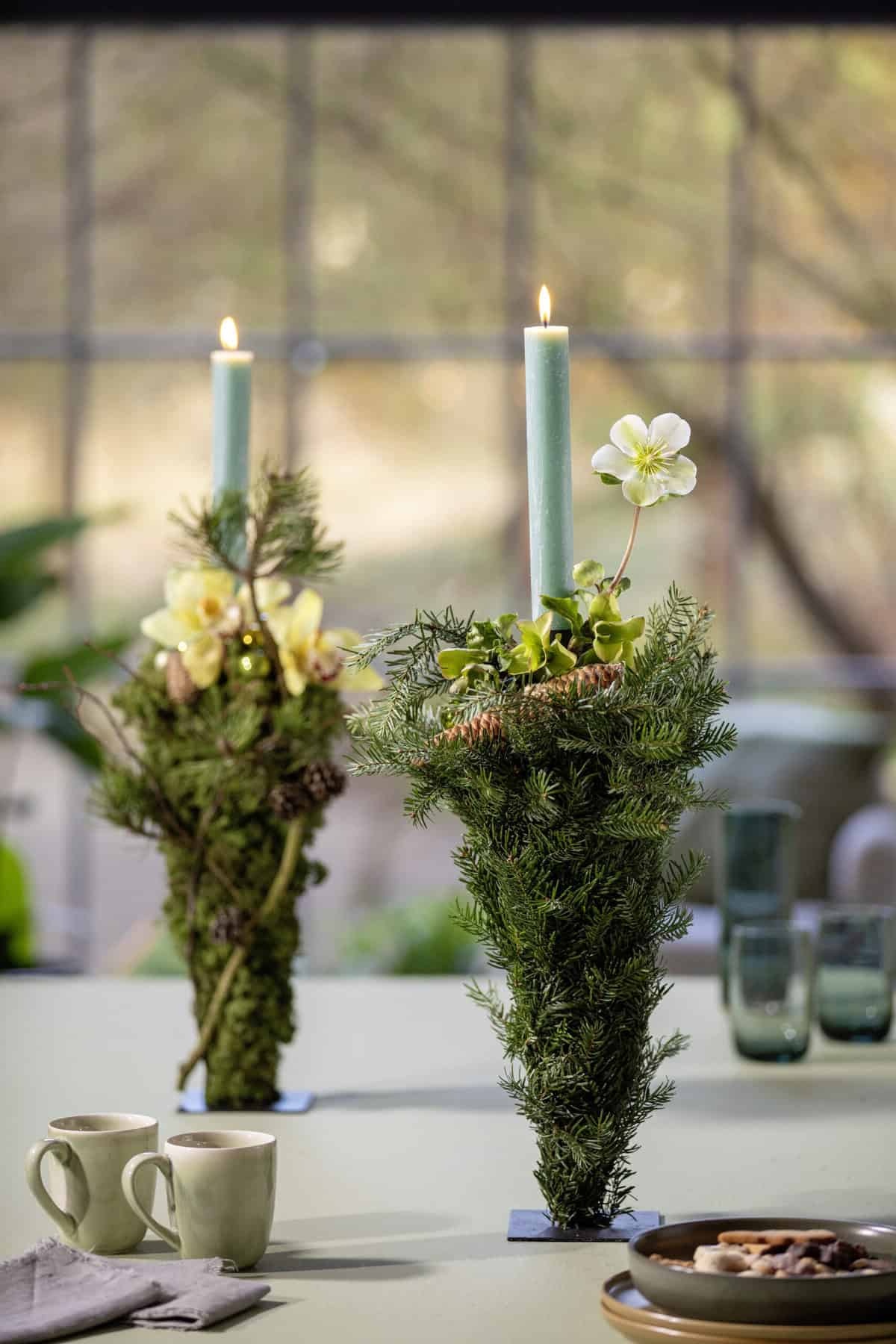 zwei Kerzen mit Tannenzweigen und Christrosen geschmückt