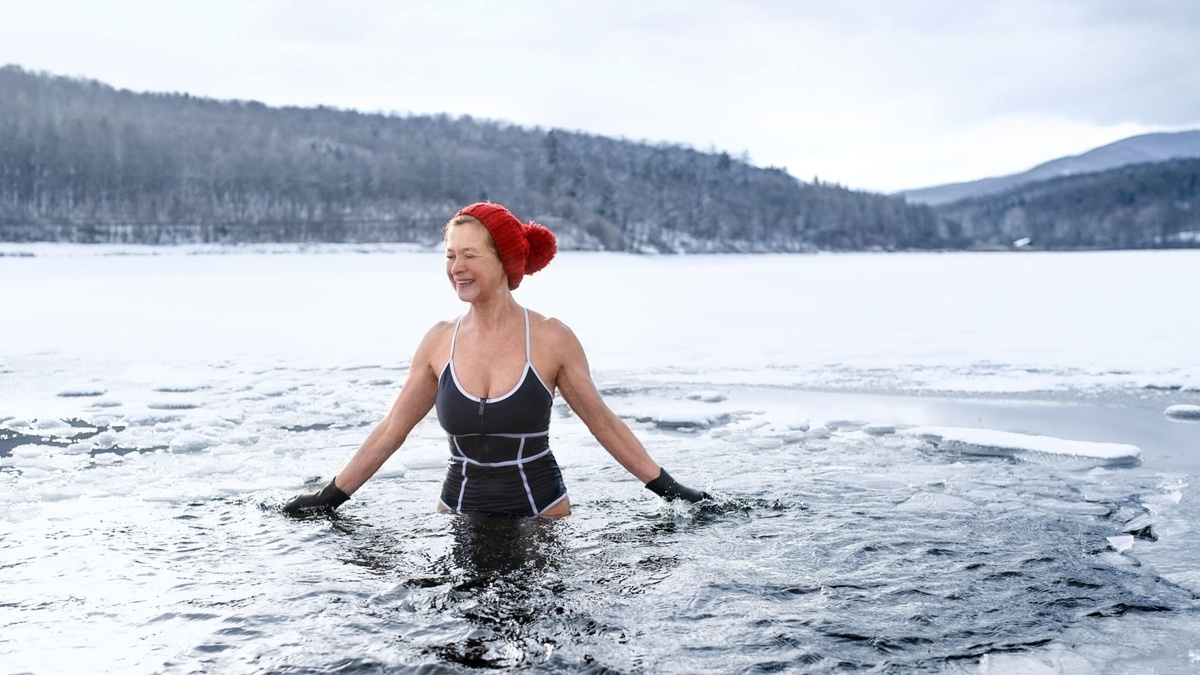 Frau im Badeanzug trägt beim Eisbaden Mütze und Handschuhe