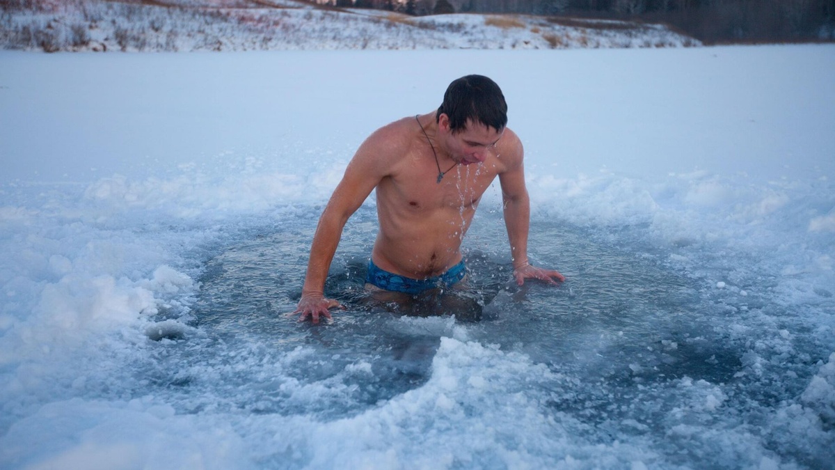 junger Mann kommt aus dem eiskalten Wasser heraus - Eisbaden im Winter
