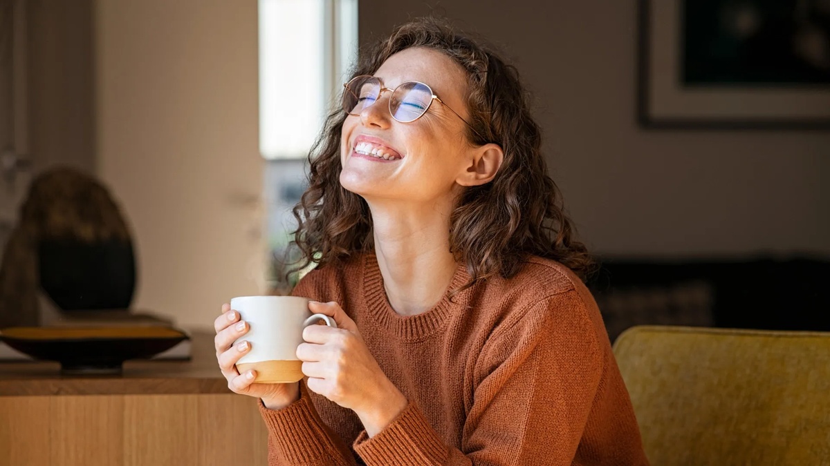 junge Frau mit Tasse Kaffee in der Hand fühlt sich glücklich