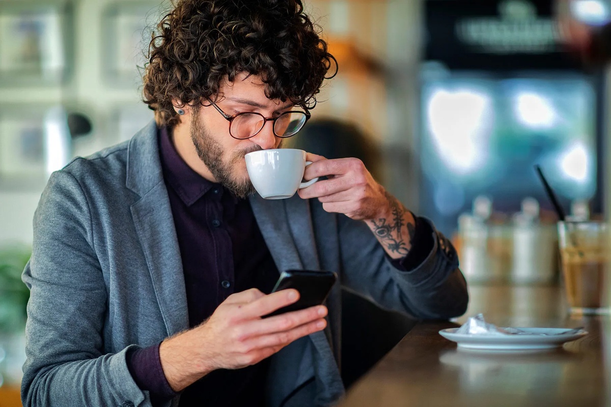 junger Mann beim Kaffee trinken - er sieht auf sein Handy